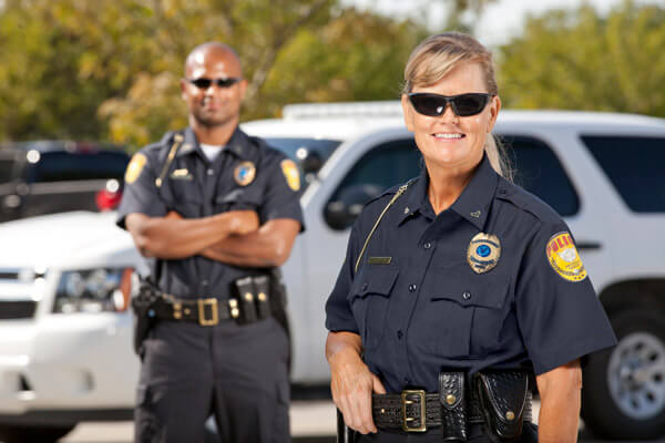 Two police officers stand in front of a car