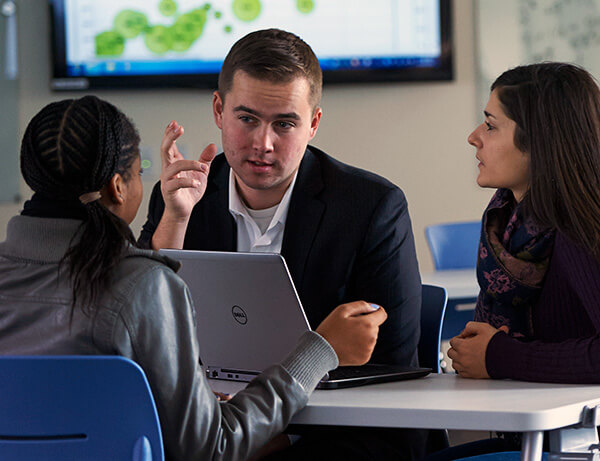 Workers talk at a table with a laptop in front of them