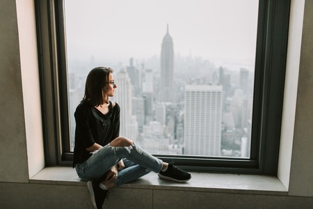 Woman sitting at a window showing the NYC skyline