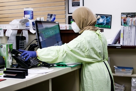 A person wearing a lab coat and mask at a computer